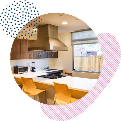 Psycho-Social Rehabilitation training kitchen – yellow chairs surrounding an island with an electric range and stainless steel hood.