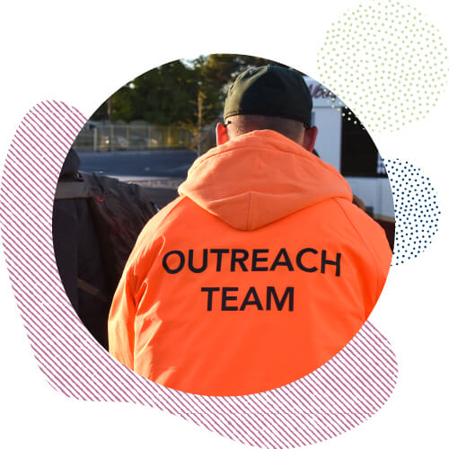 Back of Outreach worker wearing an orange jacket while handing out coffee and resources